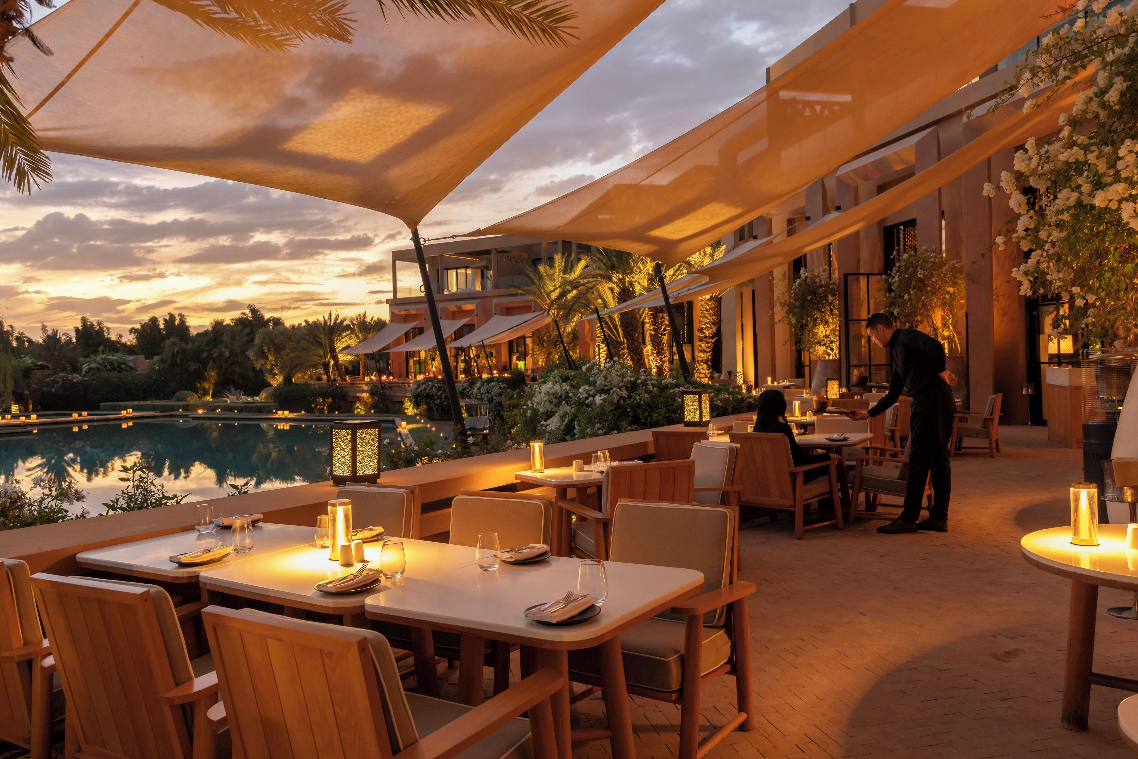 An outdoor dining area with tables and chairs, a pool, and a building with large windows.