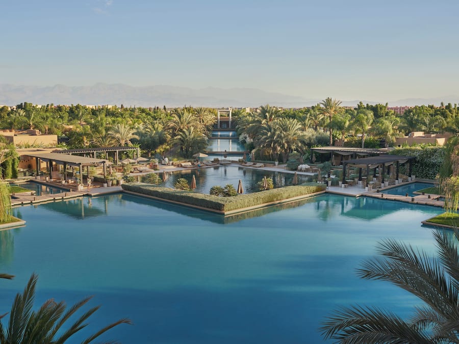 A resort with multiple swimming pools, palm trees, and a mountainous backdrop.