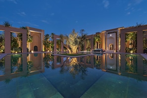 A pool reflecting a building with arched doorways and palm trees.