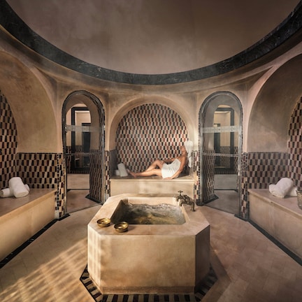 A spa room with a checkered wall pattern, a central bathtub, and a person relaxing.