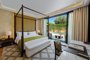 A four-poster bed with a green throw, a desk with a chair, a nightstand with a lamp, and a view of greenery through a large window. - Mandarin Oriental, Marrakech (Marrakech)