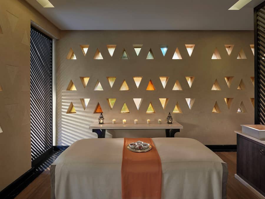 Quarto de hotel moderno com uma cama, uma mesa com velas e uma parede decorativa com recortes triangulares.