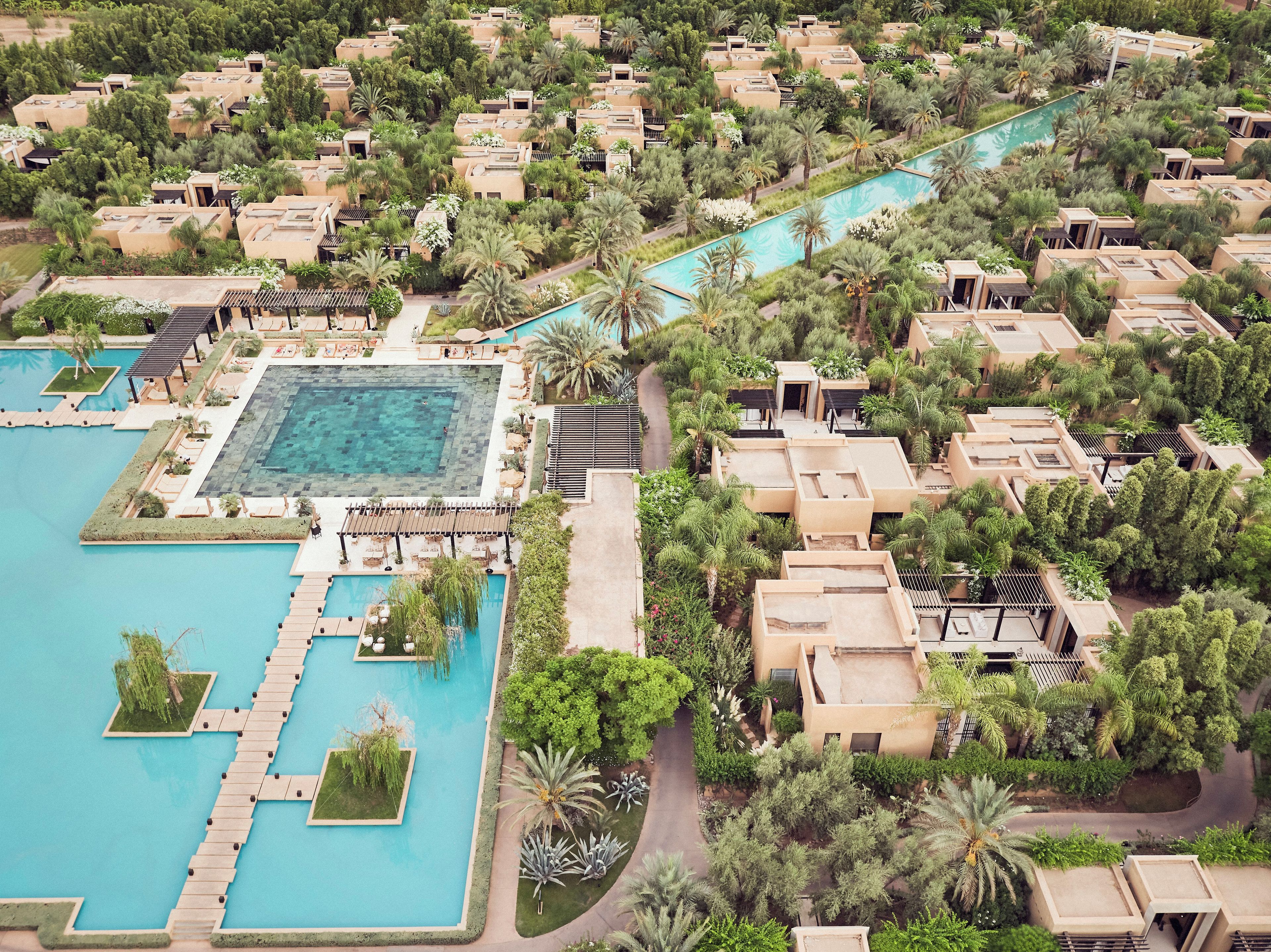 An aerial view of a resort with multiple bungalow-style accommodations, a central swimming pool, and surrounding greenery.