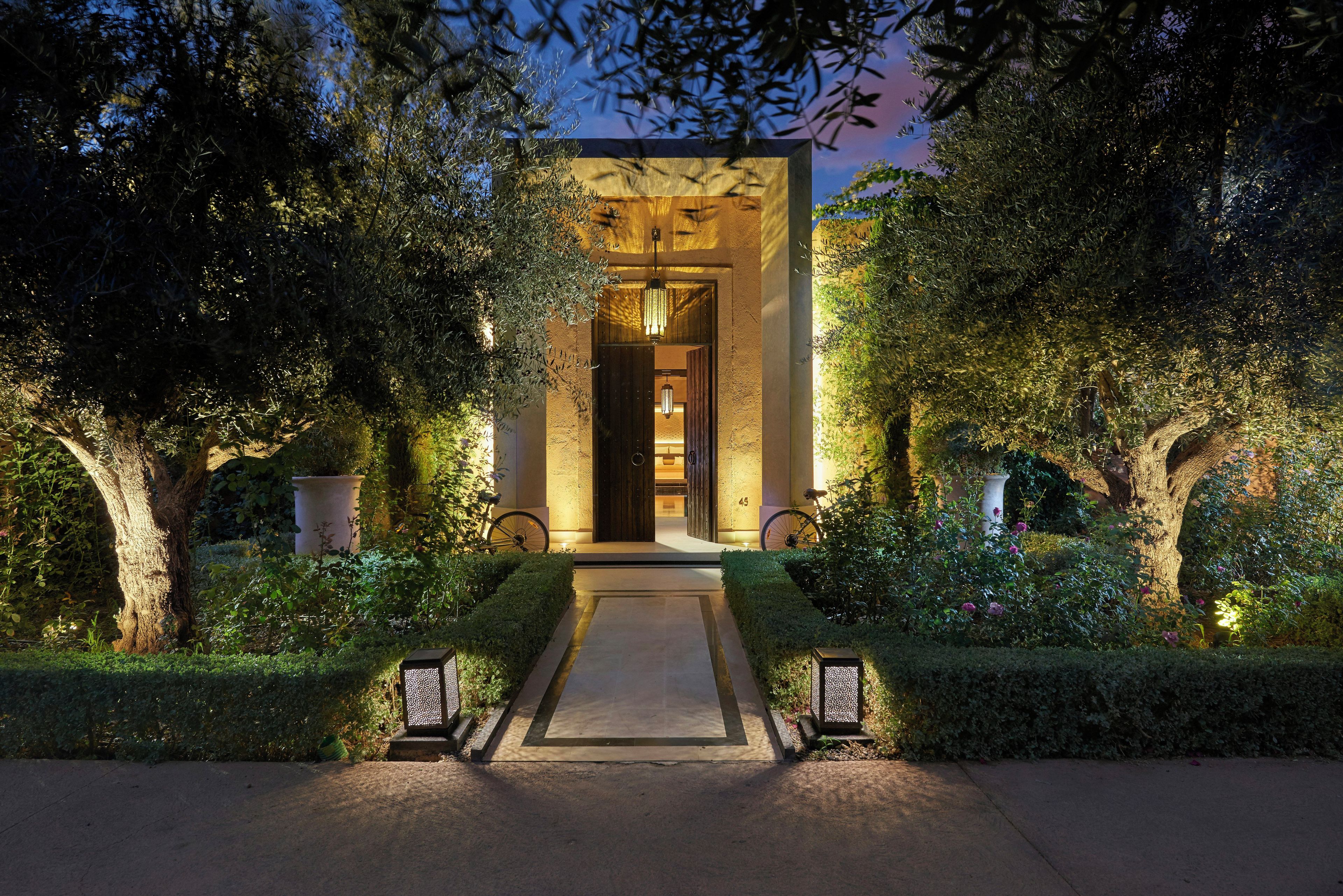 A building with a well-lit entrance, surrounded by trees and hedges.