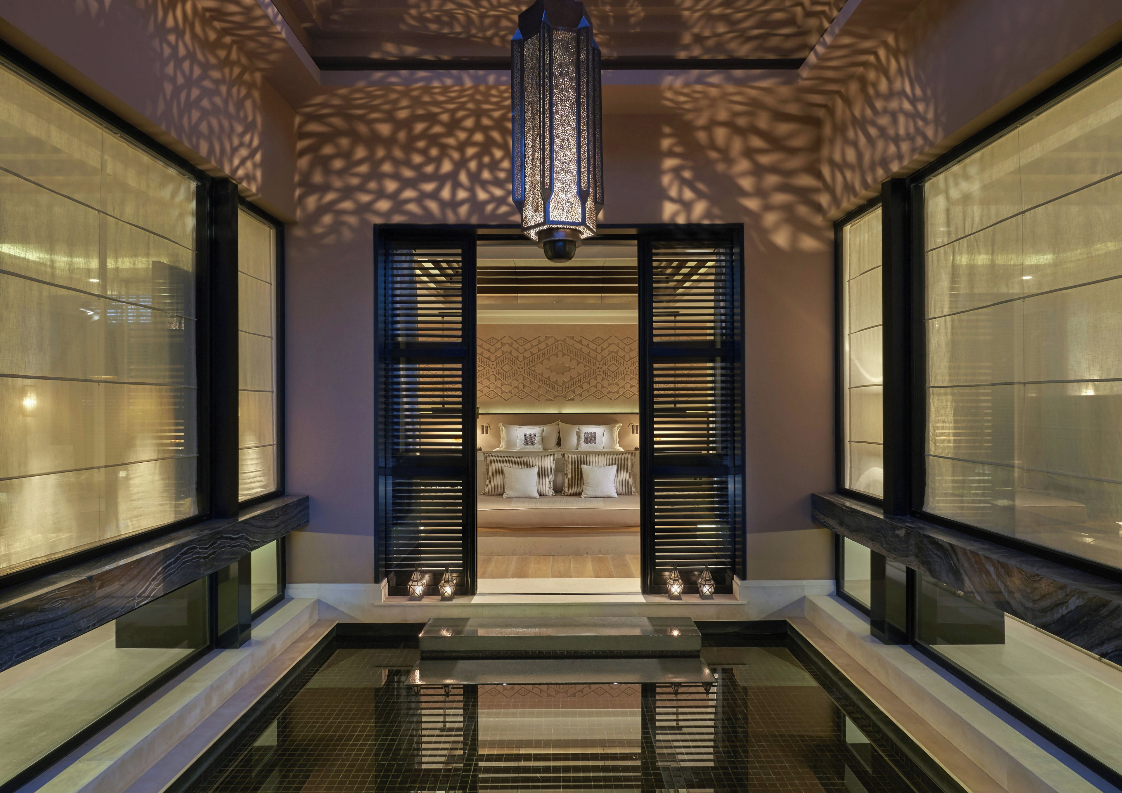 A modern hotel lobby with a central seating area, a decorative ceiling light, and a pool.