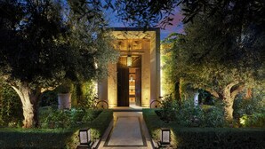 A building with a well-lit entrance, surrounded by trees and hedges. - Mandarin Oriental, Marrakech (Marrakech)