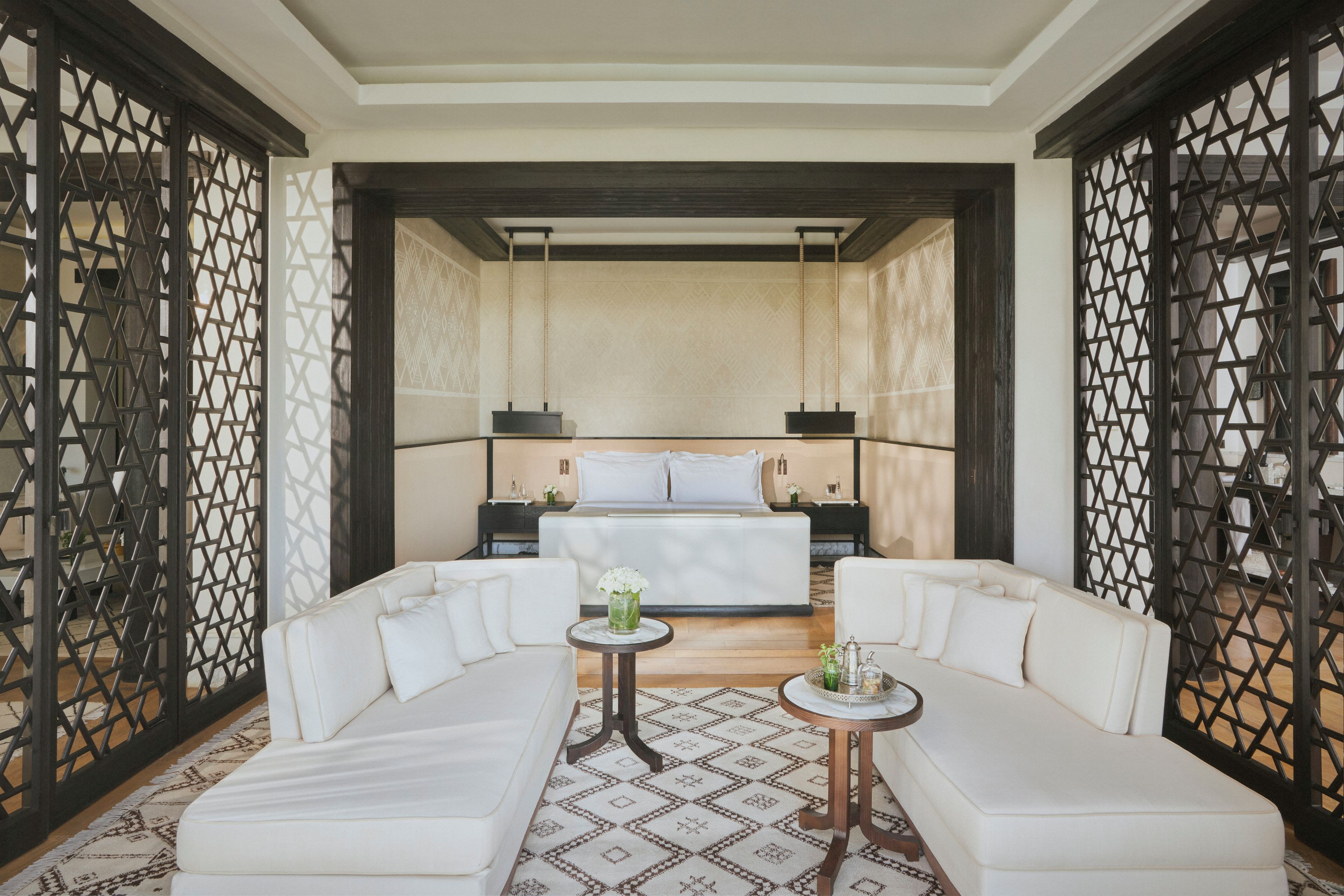 Quarto de hotel moderno com uma cama grande, dois sofás brancos, uma mesa redonda pequena e objetos decorativos.