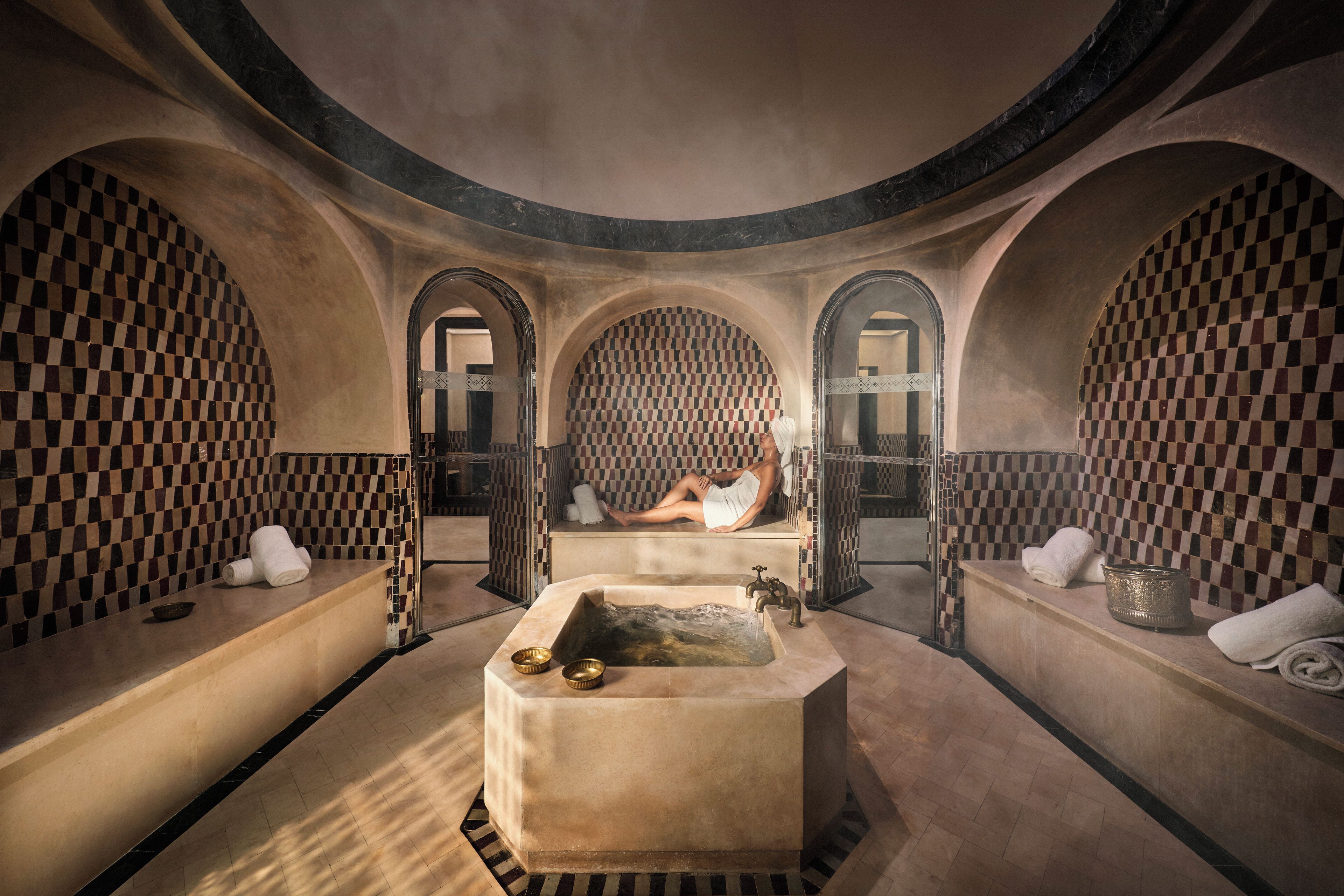 A spa room with a central bathtub, arched alcoves, checkered tiling, and towels.