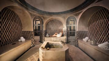 A spa room with a central bathtub, arched alcoves, checkered tiling, and towels.