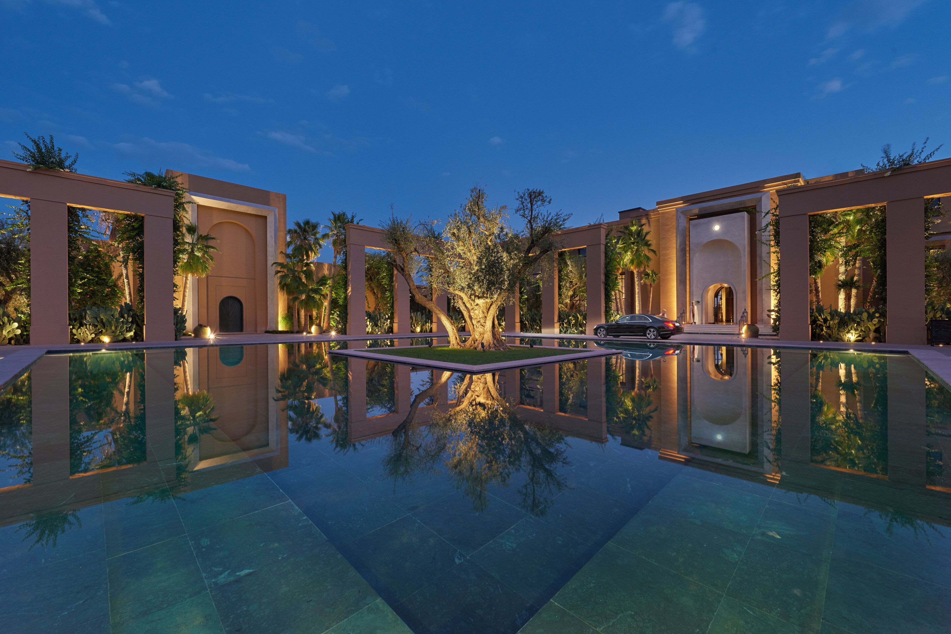 A pool reflecting a building with arched doorways and palm trees.