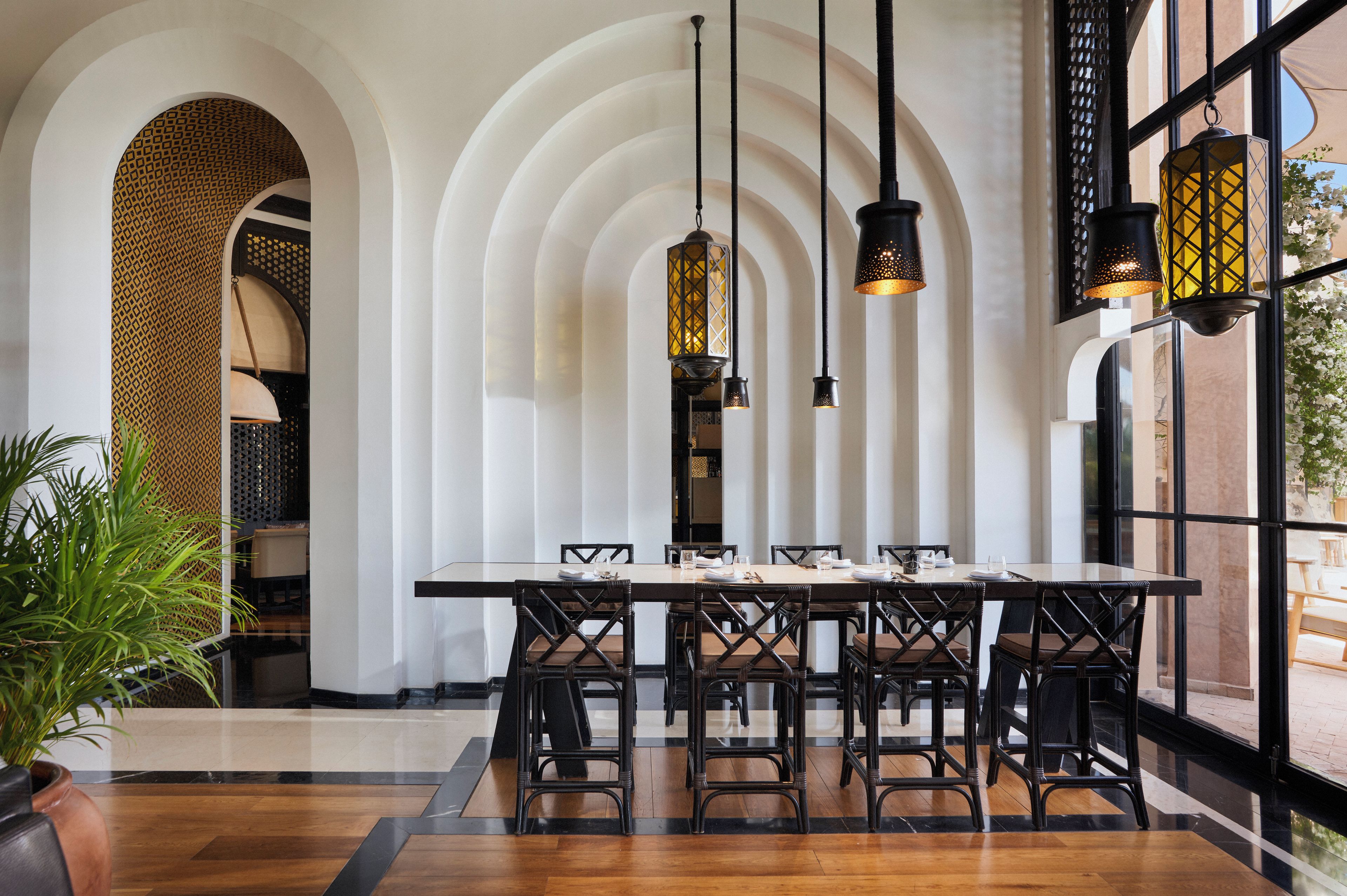 Un comedor con una mesa larga, sillas negras y lámparas colgantes.