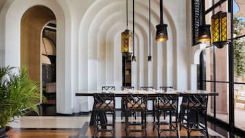 Un comedor con una mesa larga, sillas negras y lámparas colgantes.