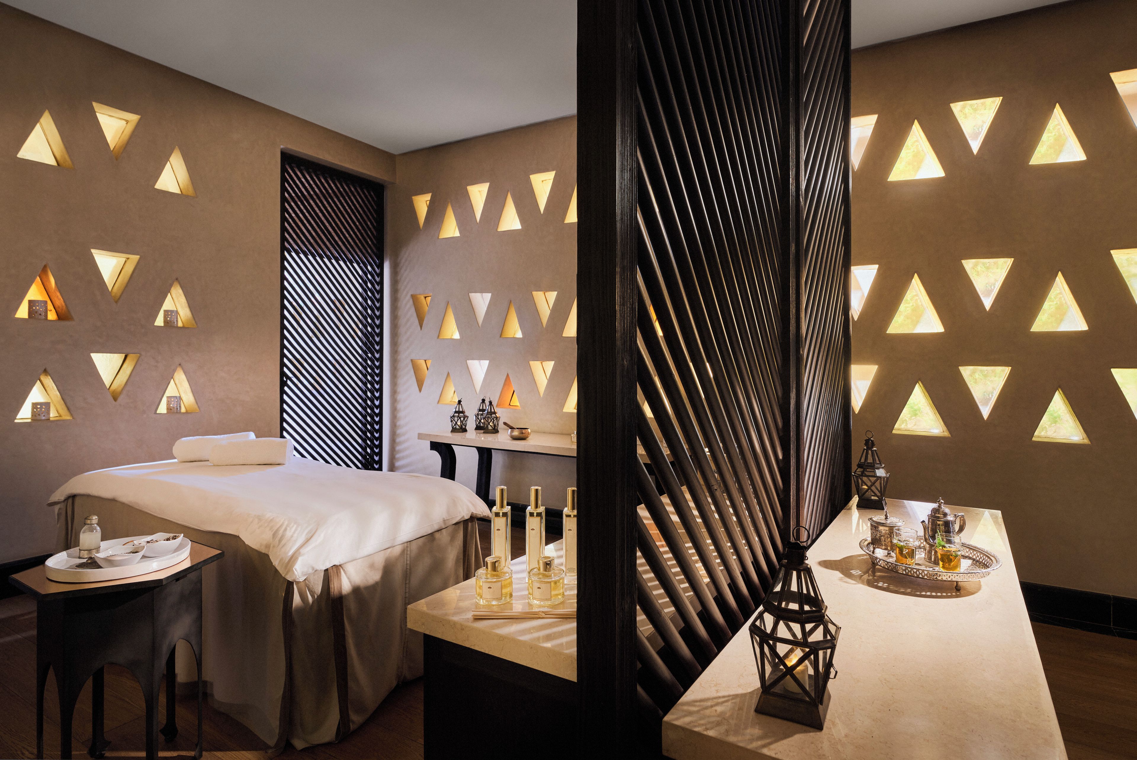 A modern room with a bed, a table with tea and glasses, and a wall with triangular light fixtures.