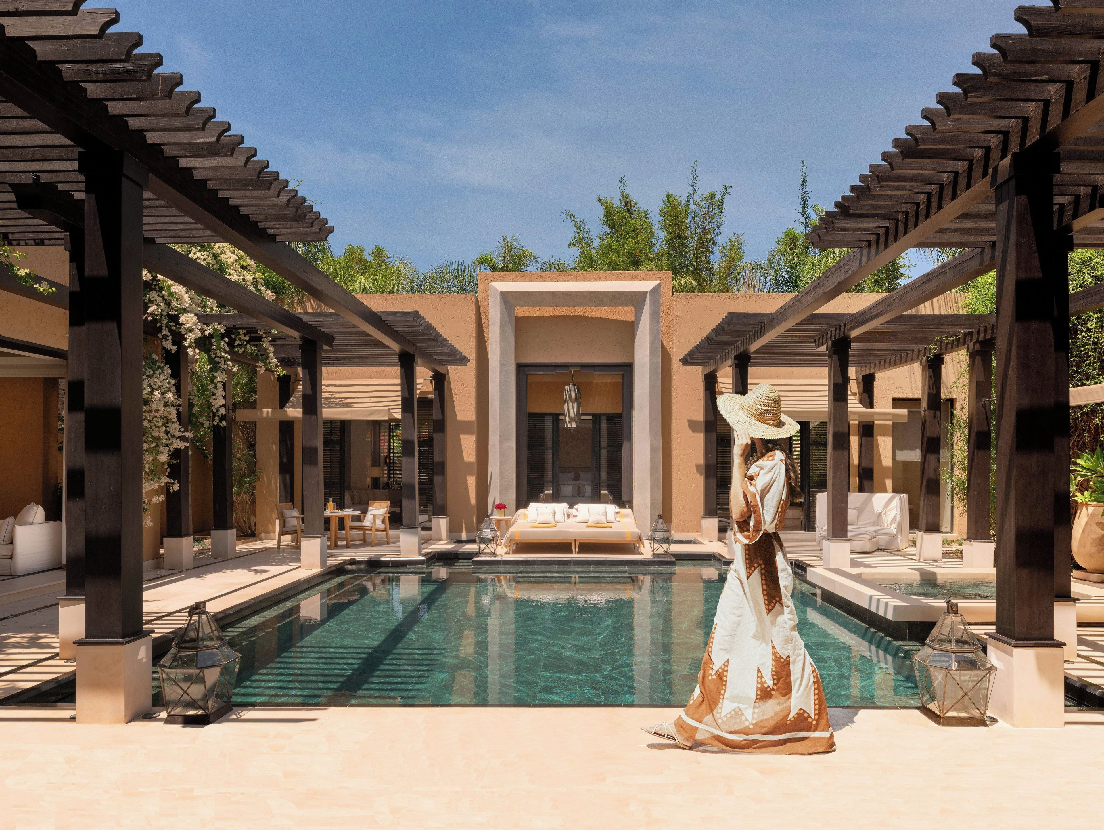 A pool area with a pergola, lounge chairs, and a person in a dress.