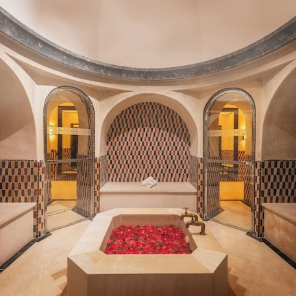 A circular room with a central bathtub filled with red flowers, benches, and checkered walls.