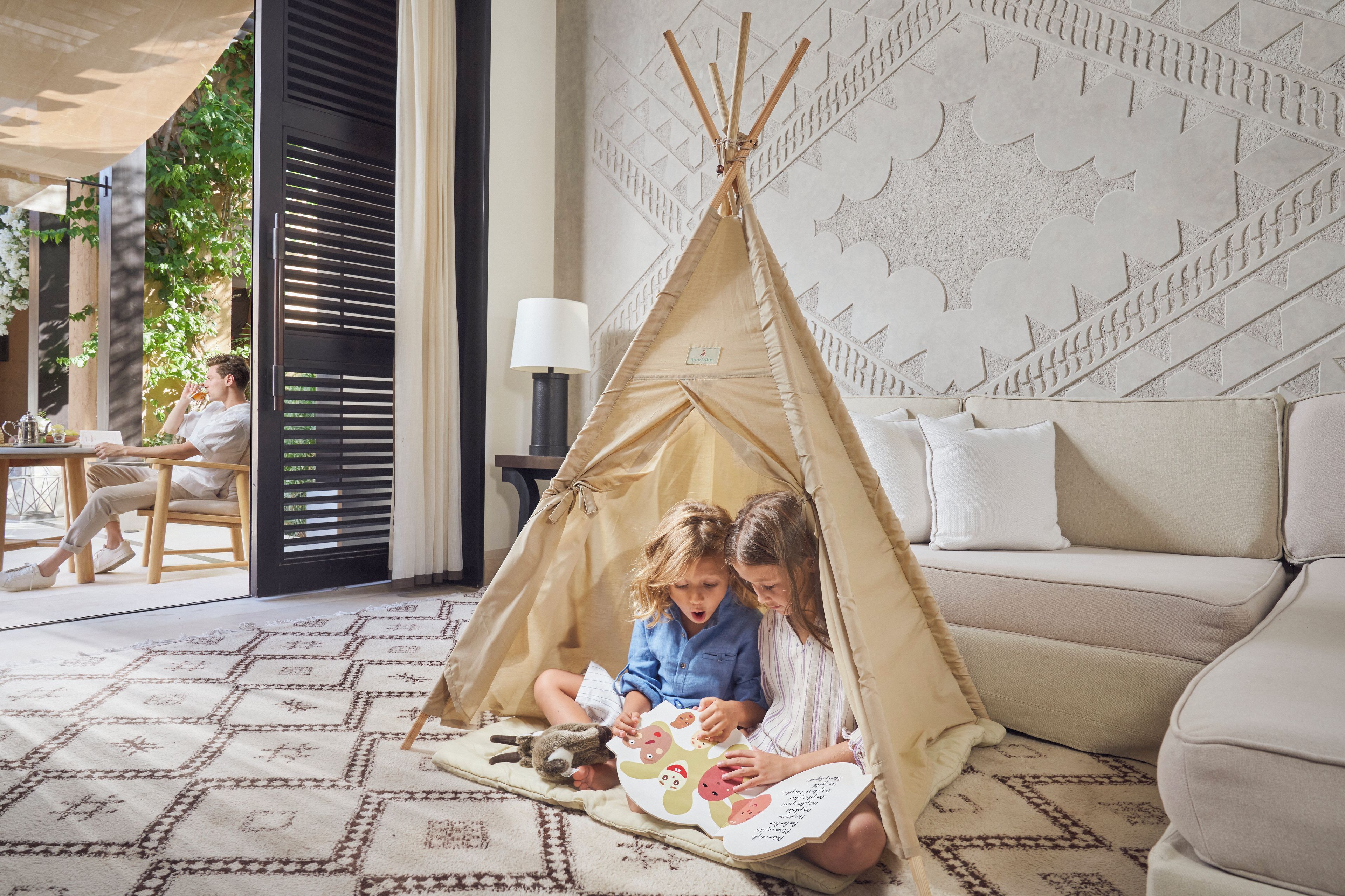 A cozy indoor setting with a teepee tent, a sofa, and a patterned rug.