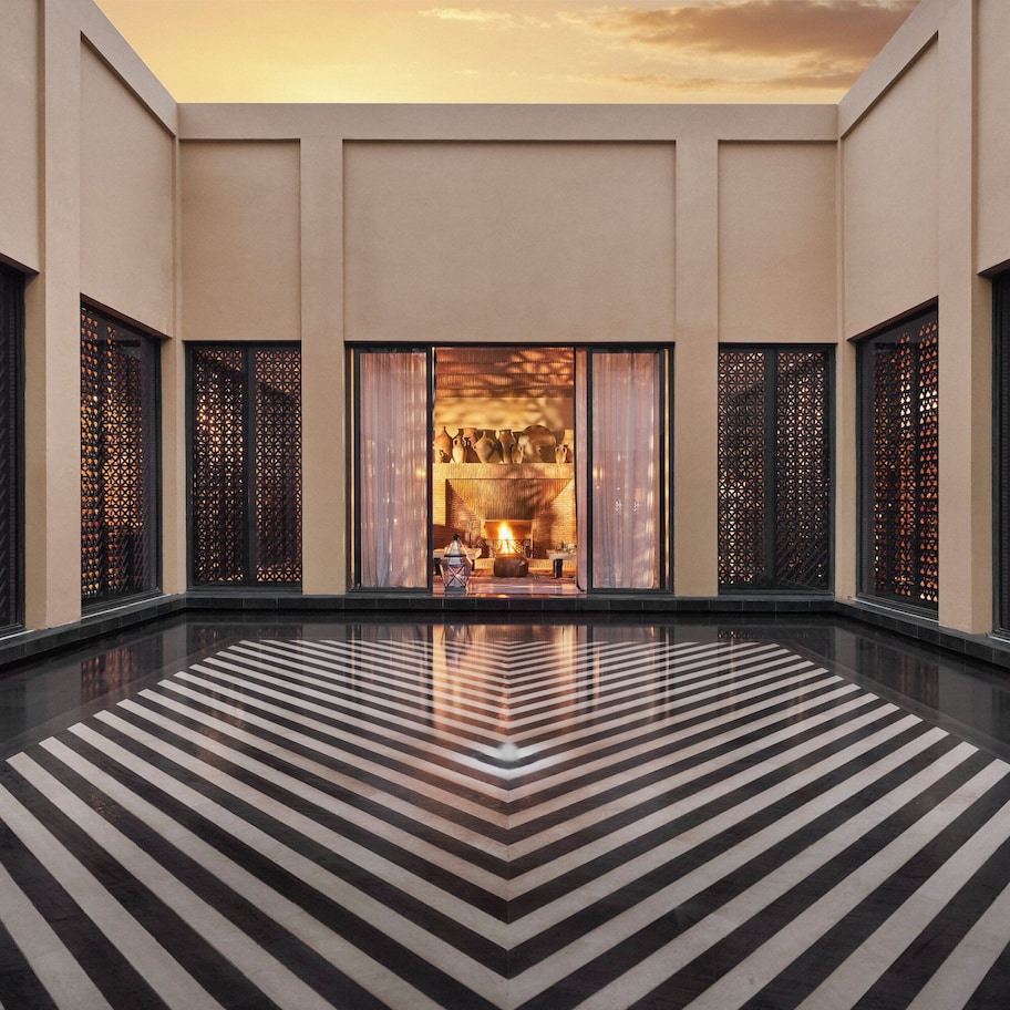 A spacious lobby with a black and white striped floor, large windows with intricate lattice designs, and a view of a warmly lit interior space.