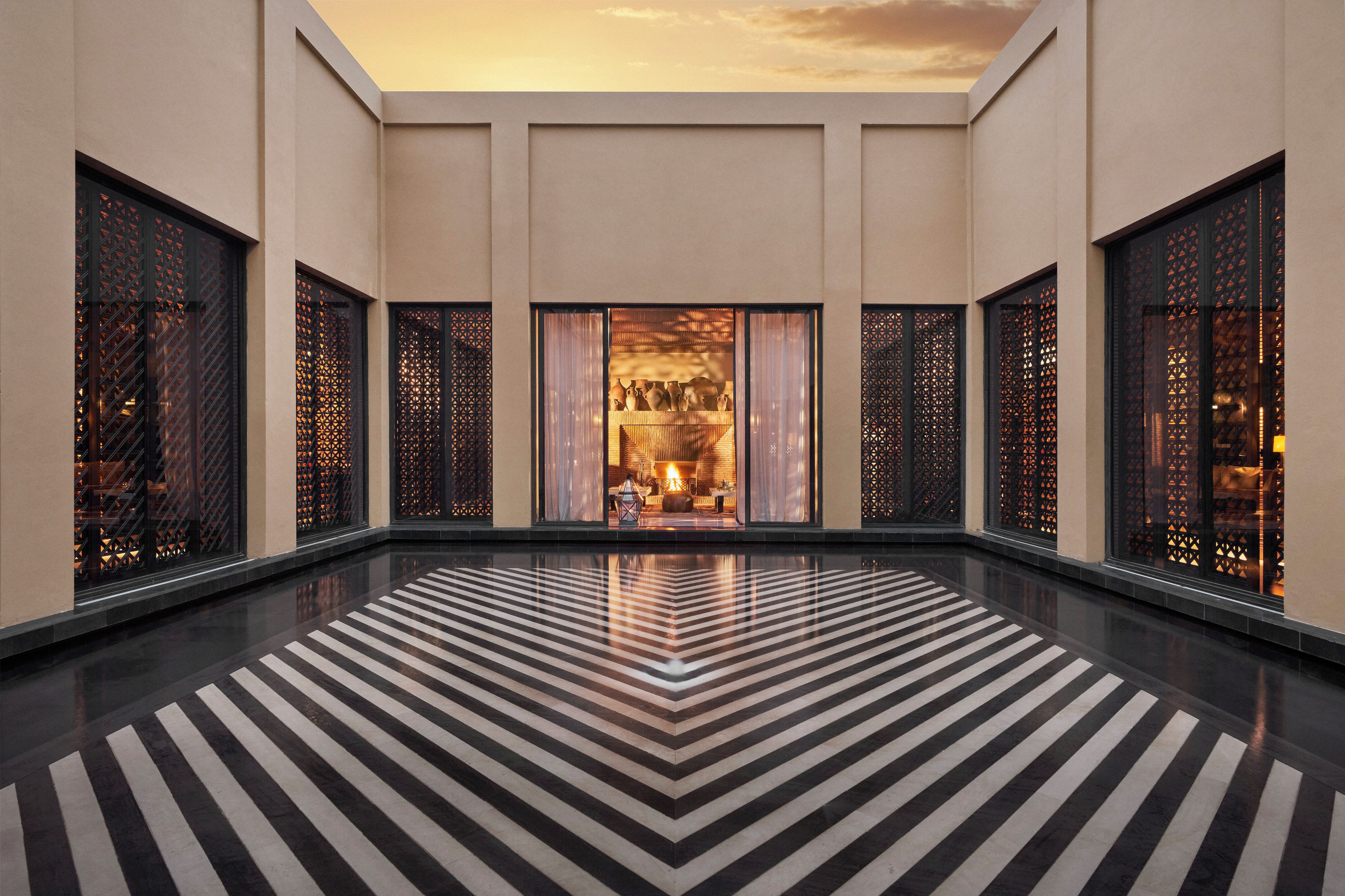 A spacious lobby with a black and white striped floor, large windows with intricate lattice designs, and a view of a warmly lit interior space.