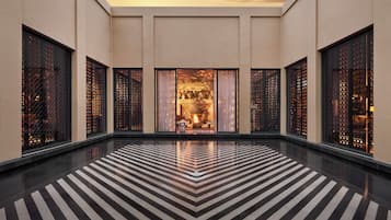 A spacious lobby with a black and white striped floor, large windows with intricate lattice designs, and a view of a warmly lit interior space.