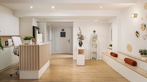 A modern reception area with a wooden reception desk, a white wall-mounted sign, and a hallway leading to a door. - BYPILLOW House (Barcelona)