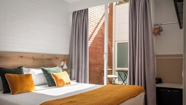 A modern bedroom with a brick wall, a large bed with multiple pillows, and a view of a balcony. - BYPILLOW House (Barcelona)