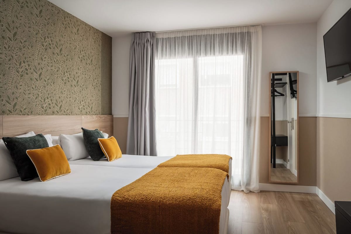 A hotel room with a bed, a bench, a wardrobe, and a television.
