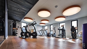 Un gimnasio con equipo de ejercicio, ventanas amplias y piso de madera.