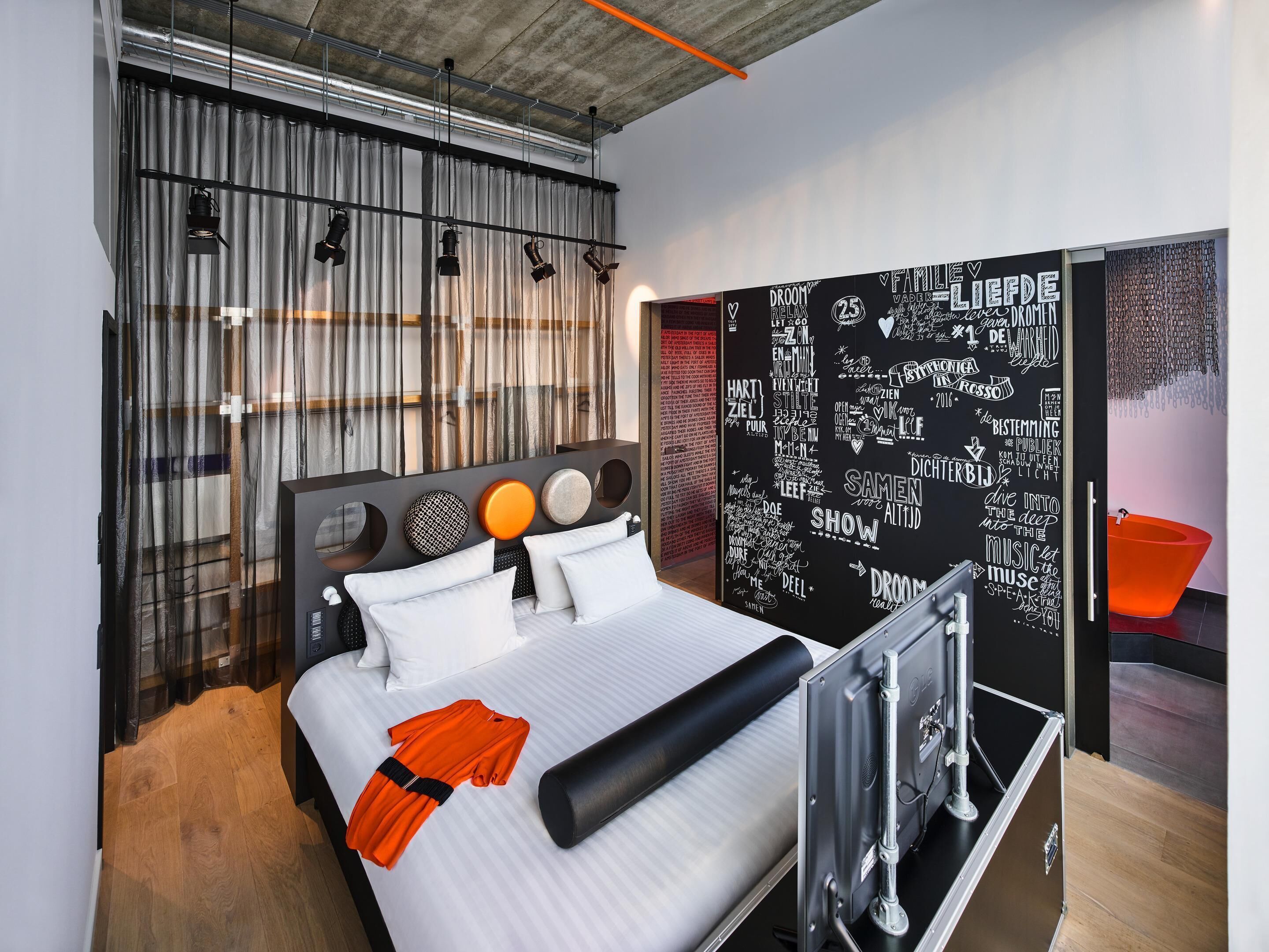 Una habitación de hotel moderna con una cama grande, una pared negra con texto blanco y una cortina con estampado a rayas.