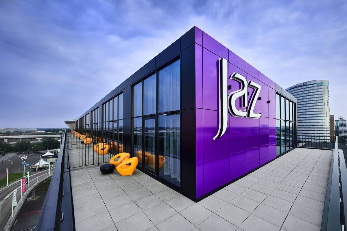 A modern building with large glass windows and a purple facade, surrounded by a cityscape.
