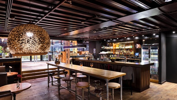 Zona de bar con taburetes, una barra de madera y una lámpara colgante.