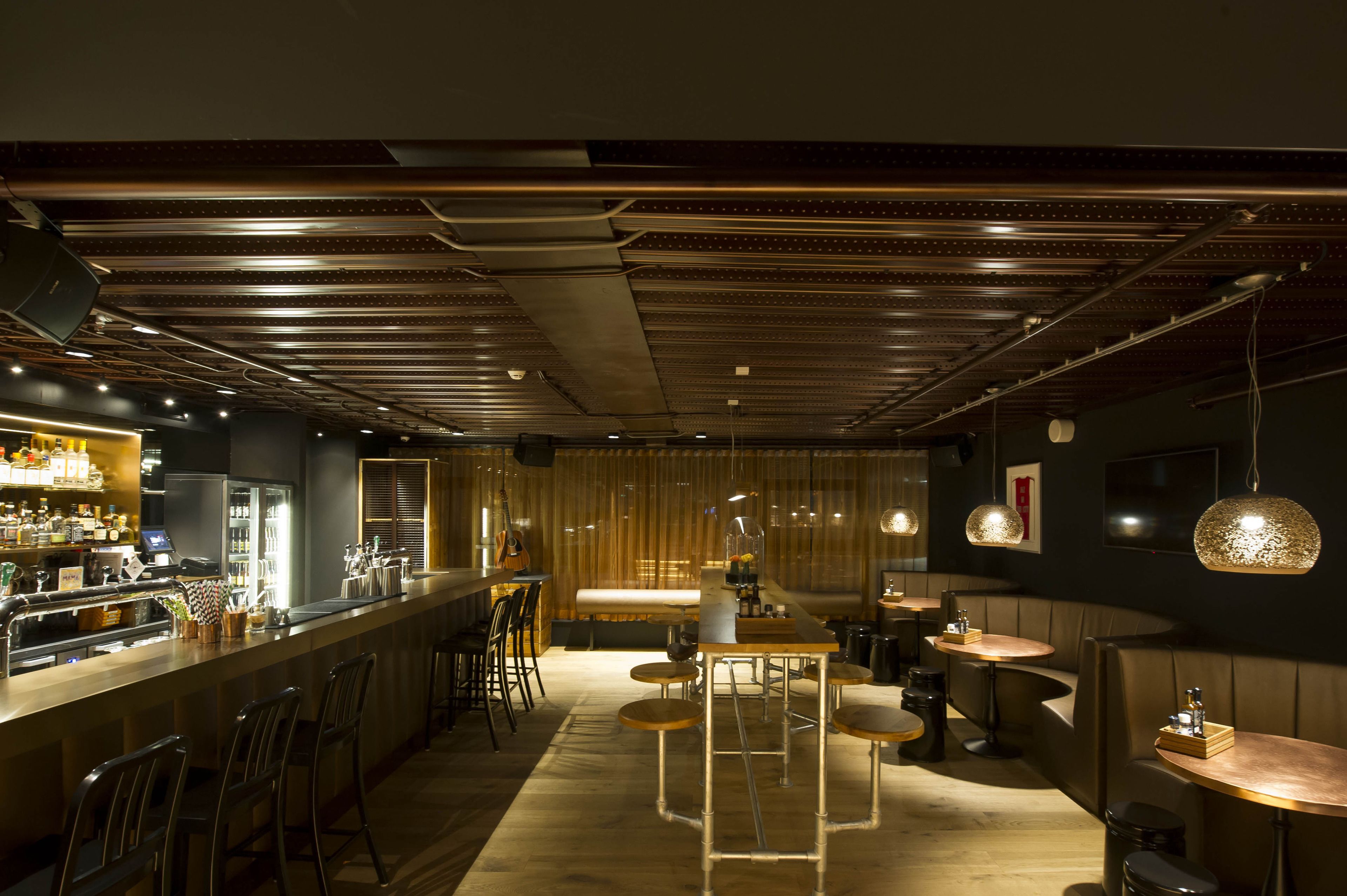 Een moderne bar met een lange toonbank, krukken en hanglampen.