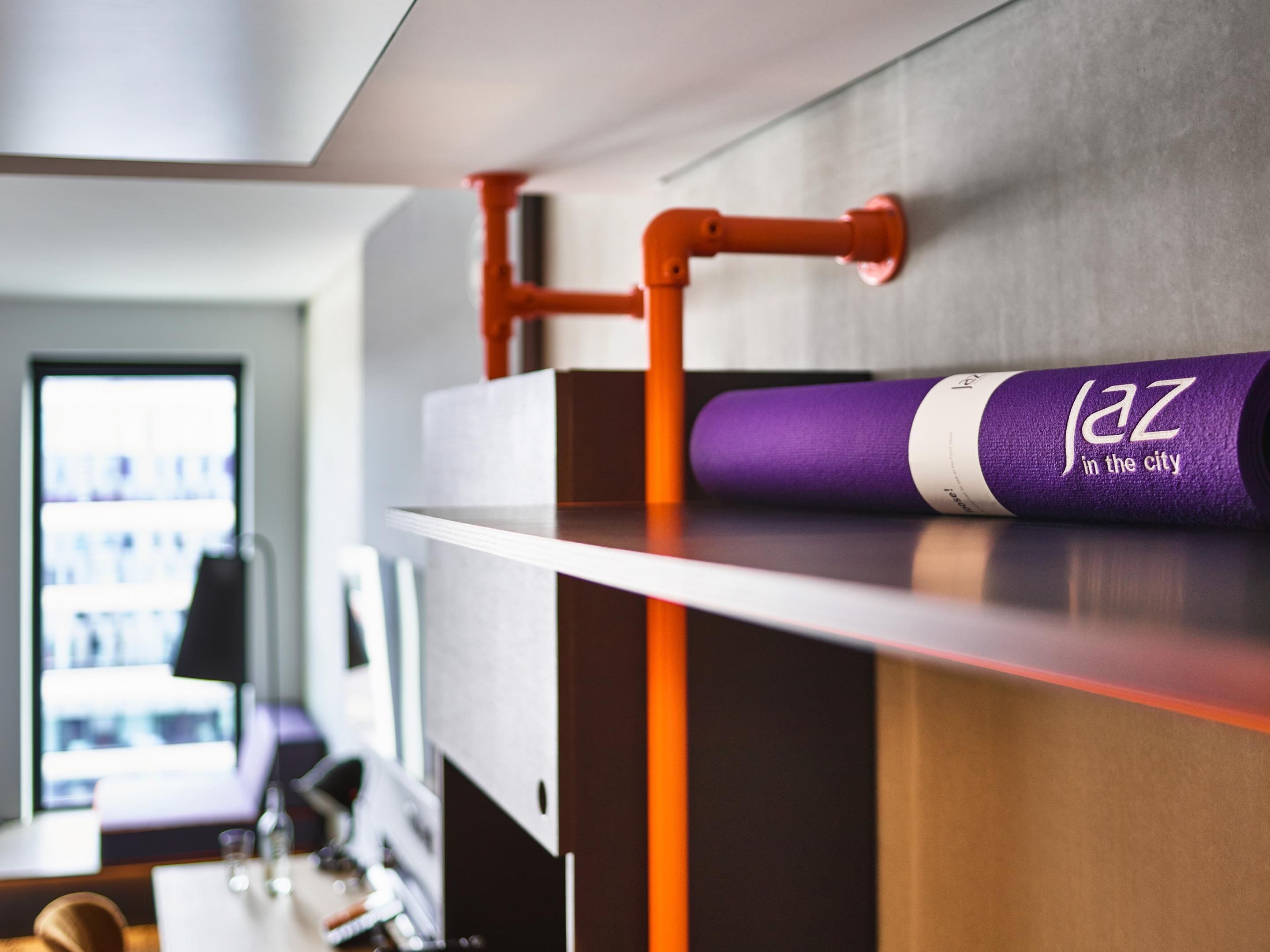 A modern hotel room with a built-in shelf, a purple yoga mat, and a window with a view.