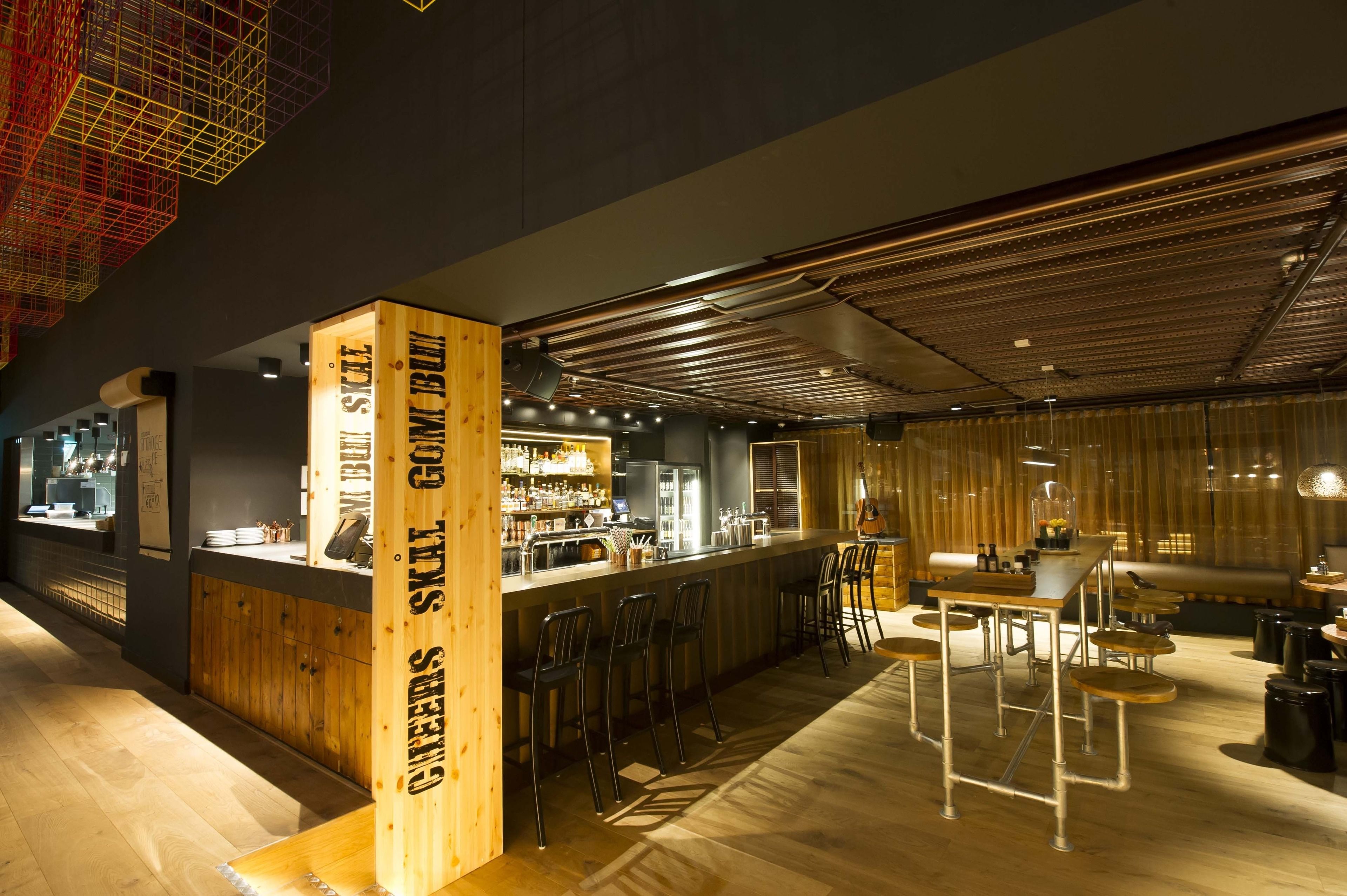 A modern bar area with wooden accents, bar stools, and a counter with a menu.