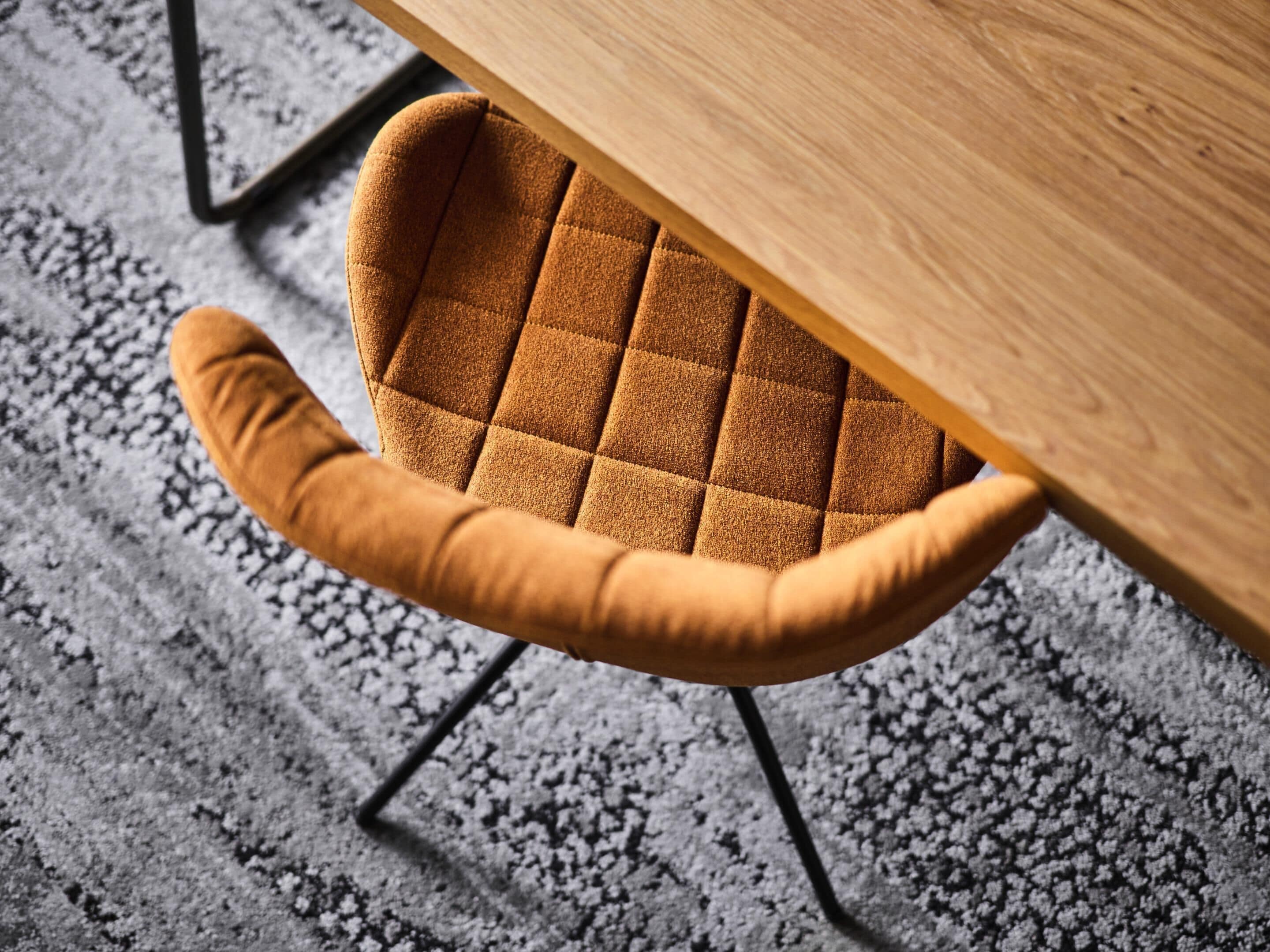 Uma cadeira com assento e encosto acolchoados, colocada sob uma mesa de madeira.