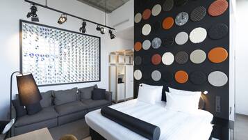 Una camera d'albergo moderna con un letto grande, un divano grigio, una scrivania con una lampada e una parete decorata con motivi circolari.