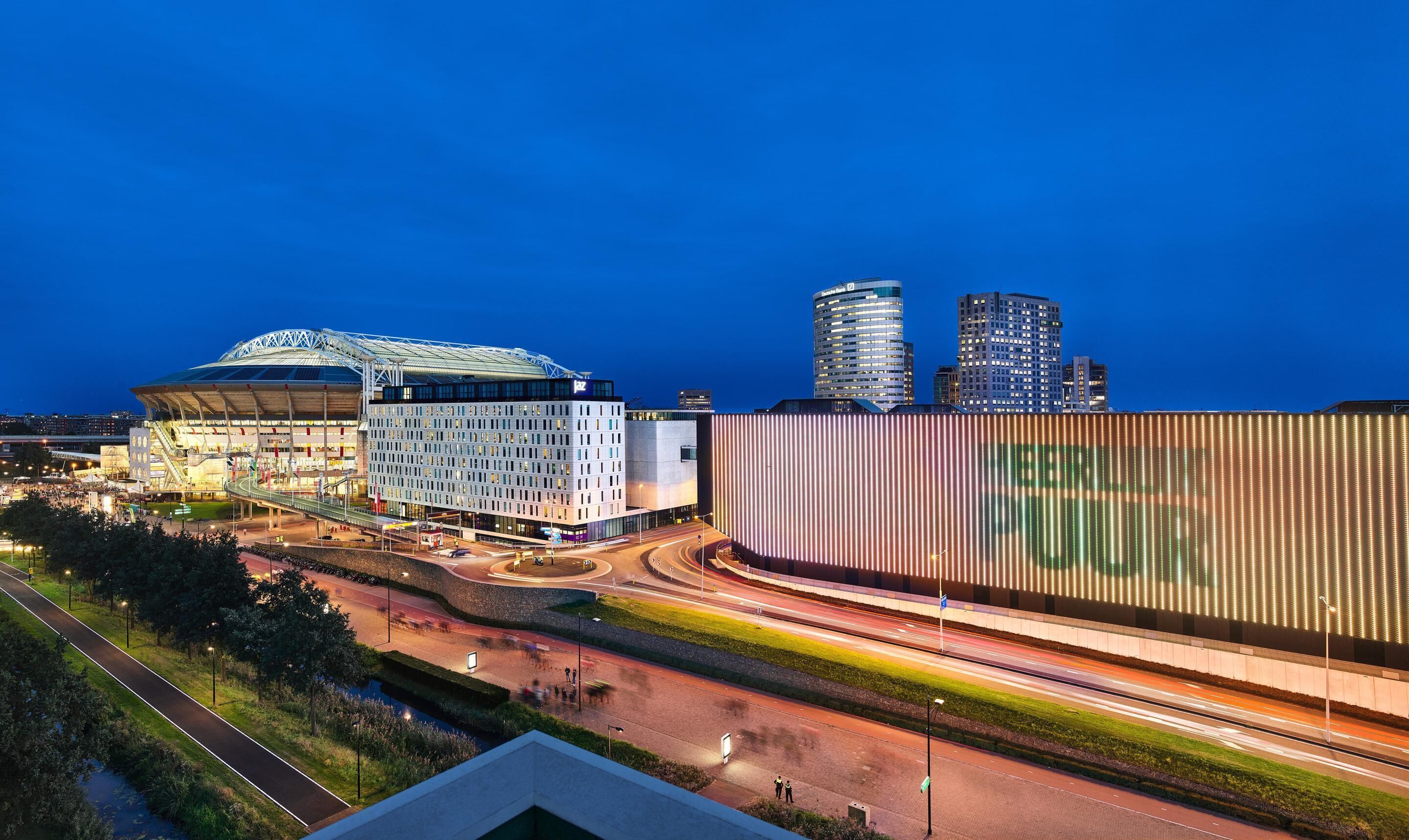 Een stadion, een modern gebouw en hoogbouw in de schemering.