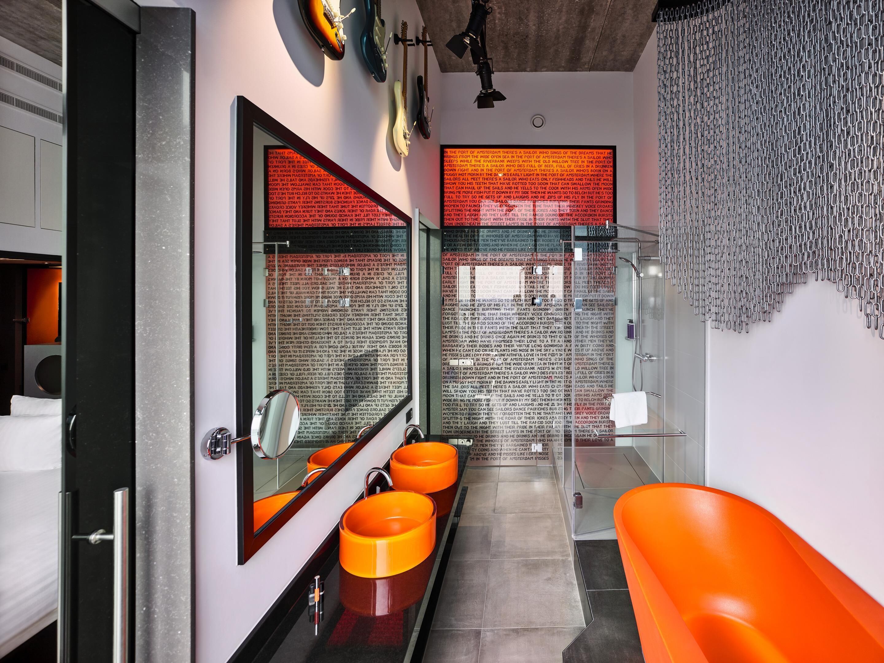A modern bathroom with a glass shower enclosure, a large mirror, and three orange sinks.