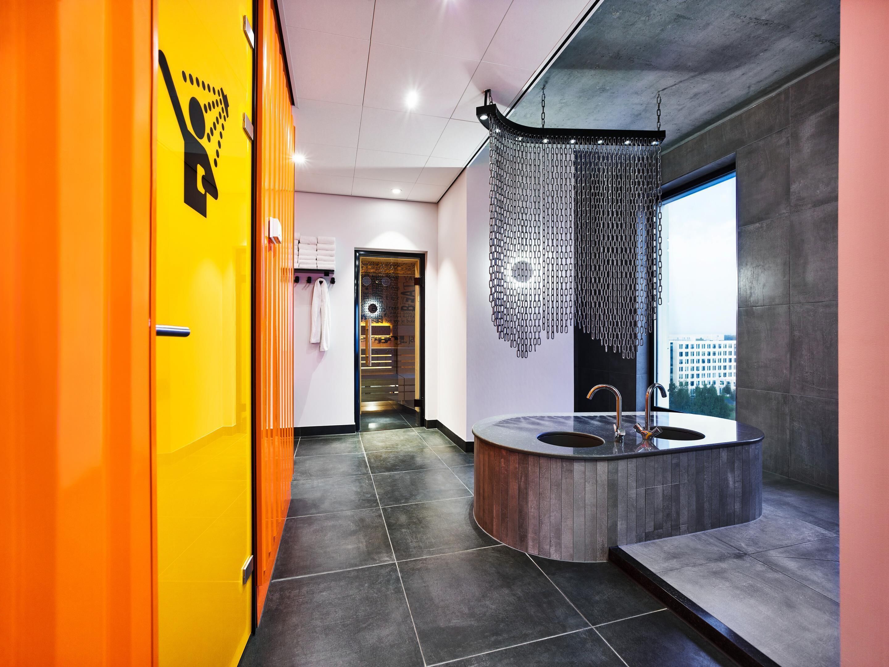A modern bathroom with a large sink, a shower area, and a view of the city.