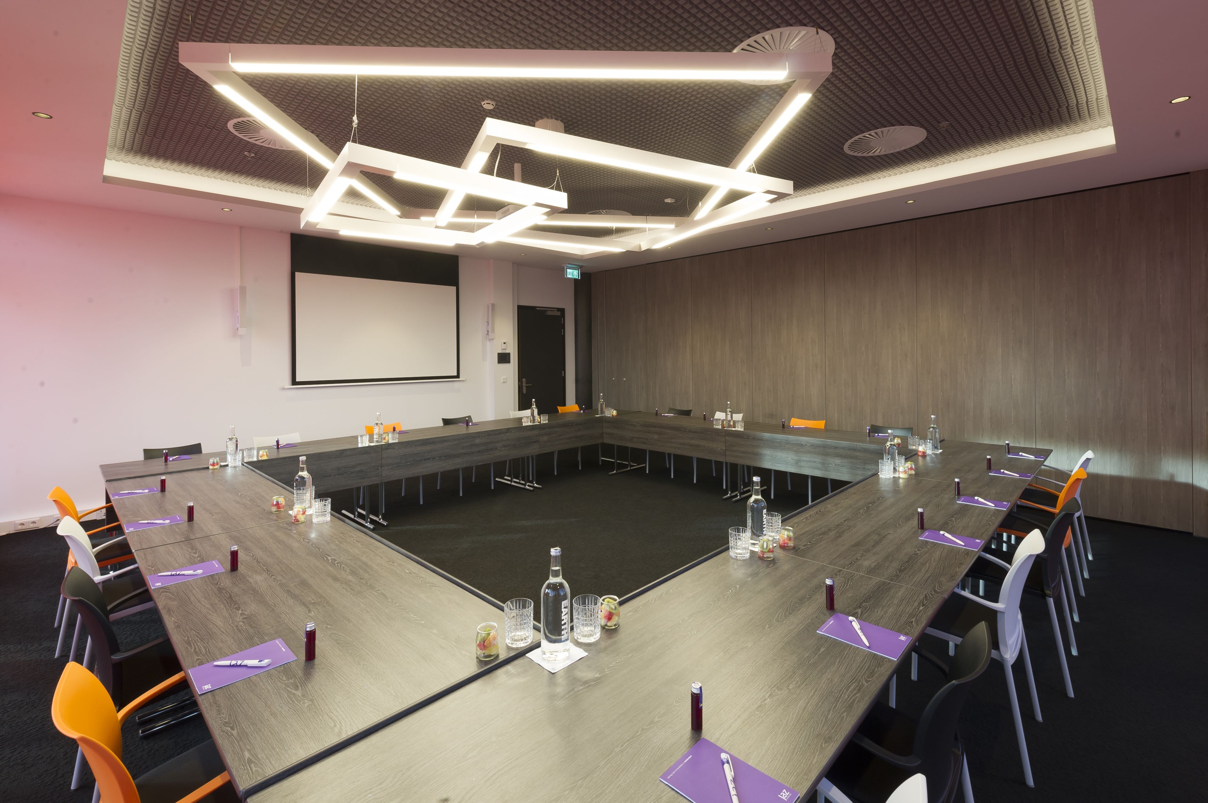 Een vergaderruimte met een lange tafel, stoelen en een scherm voor een beamer.
