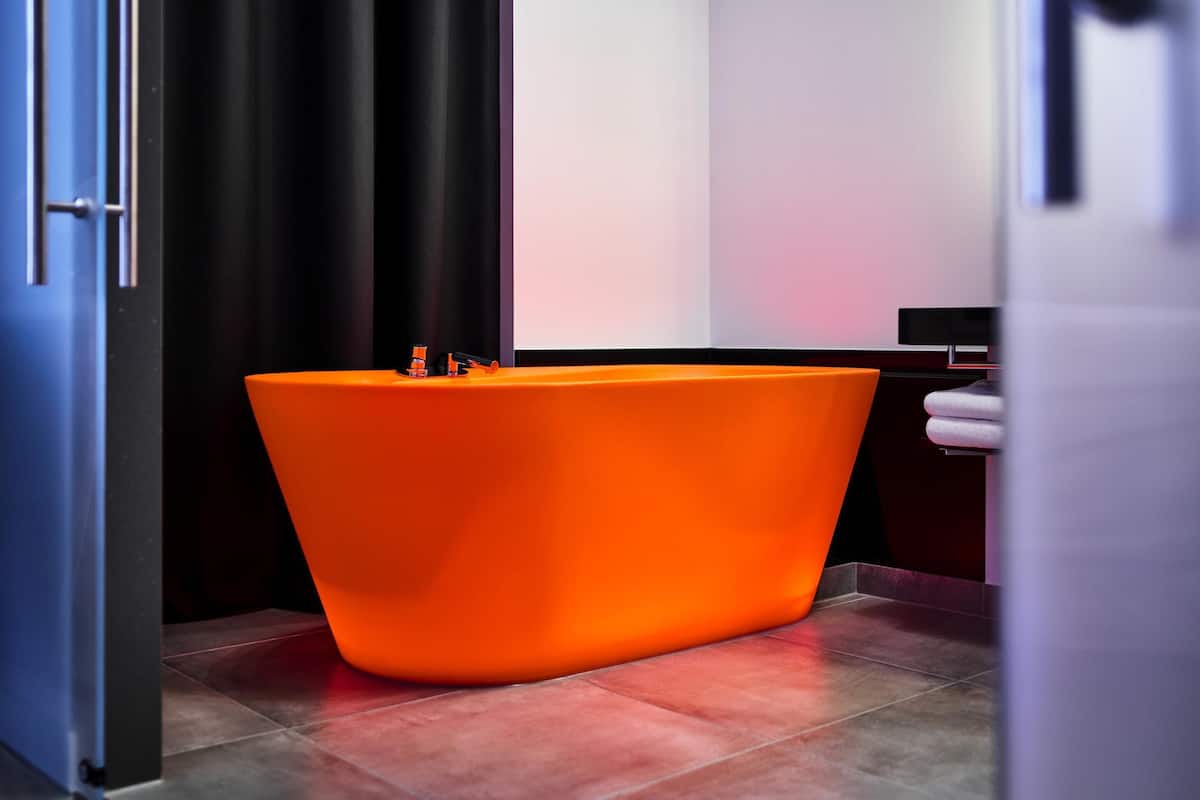 A modern bathroom with a large, orange bathtub, a door, and a towel rack.