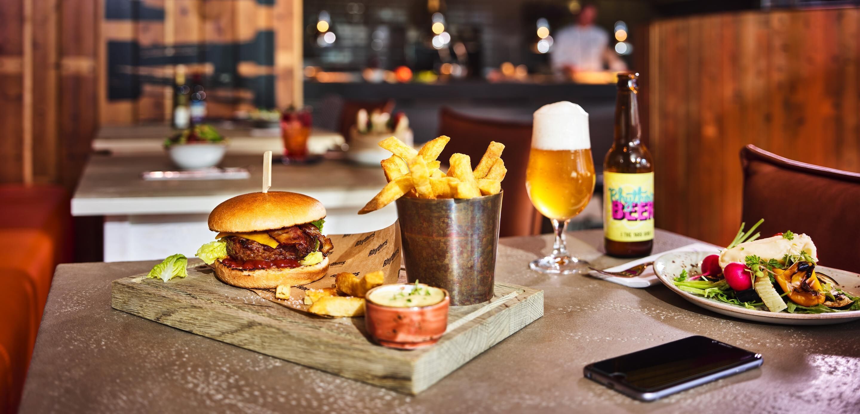 A restaurant setting with a burger, fries, beer, and a salad on the table.