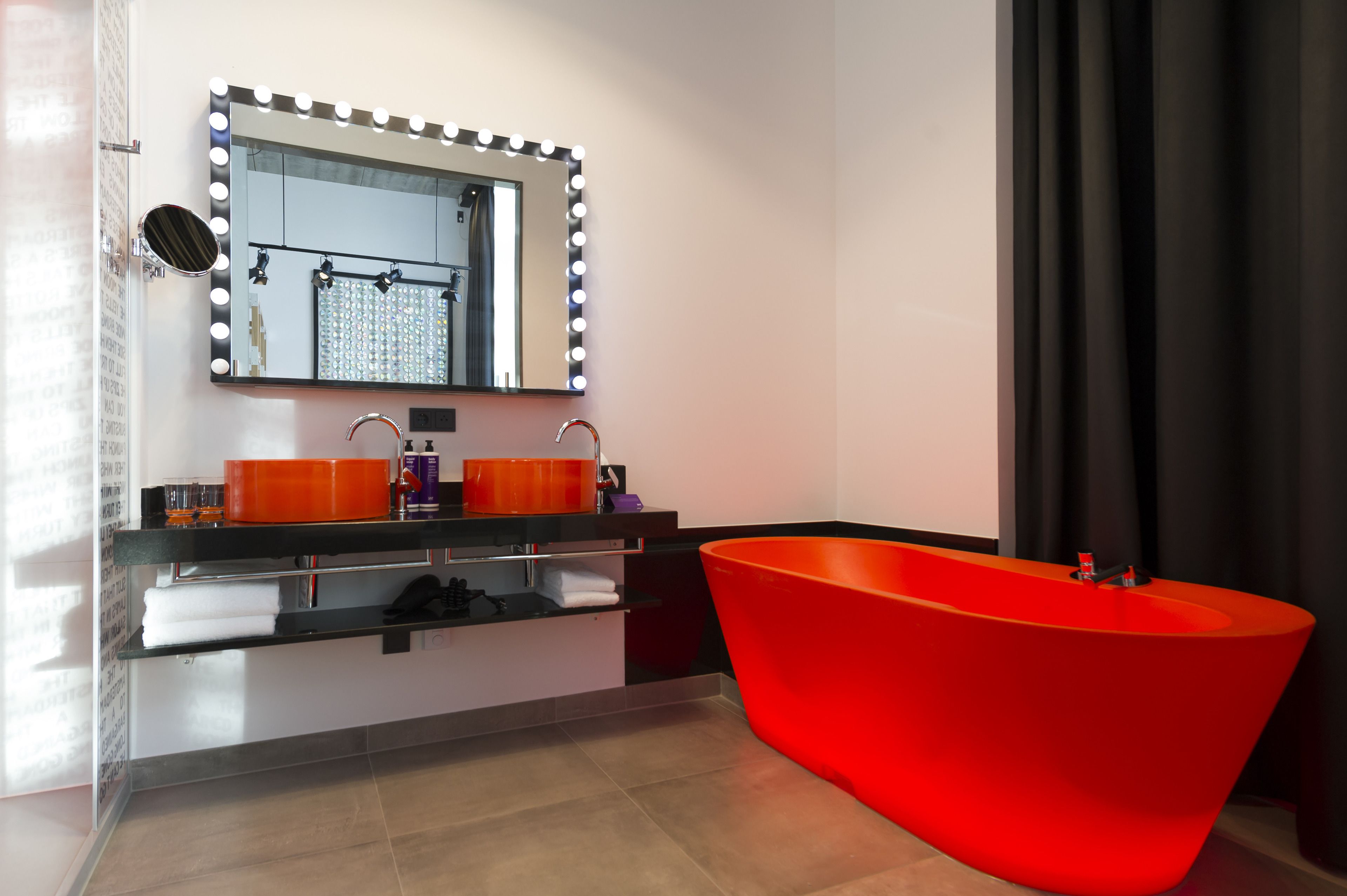 Ein modernes Badezimmer mit einer roten Badewanne, einem Waschtisch mit zwei Becken und einem beleuchteten Spiegel.