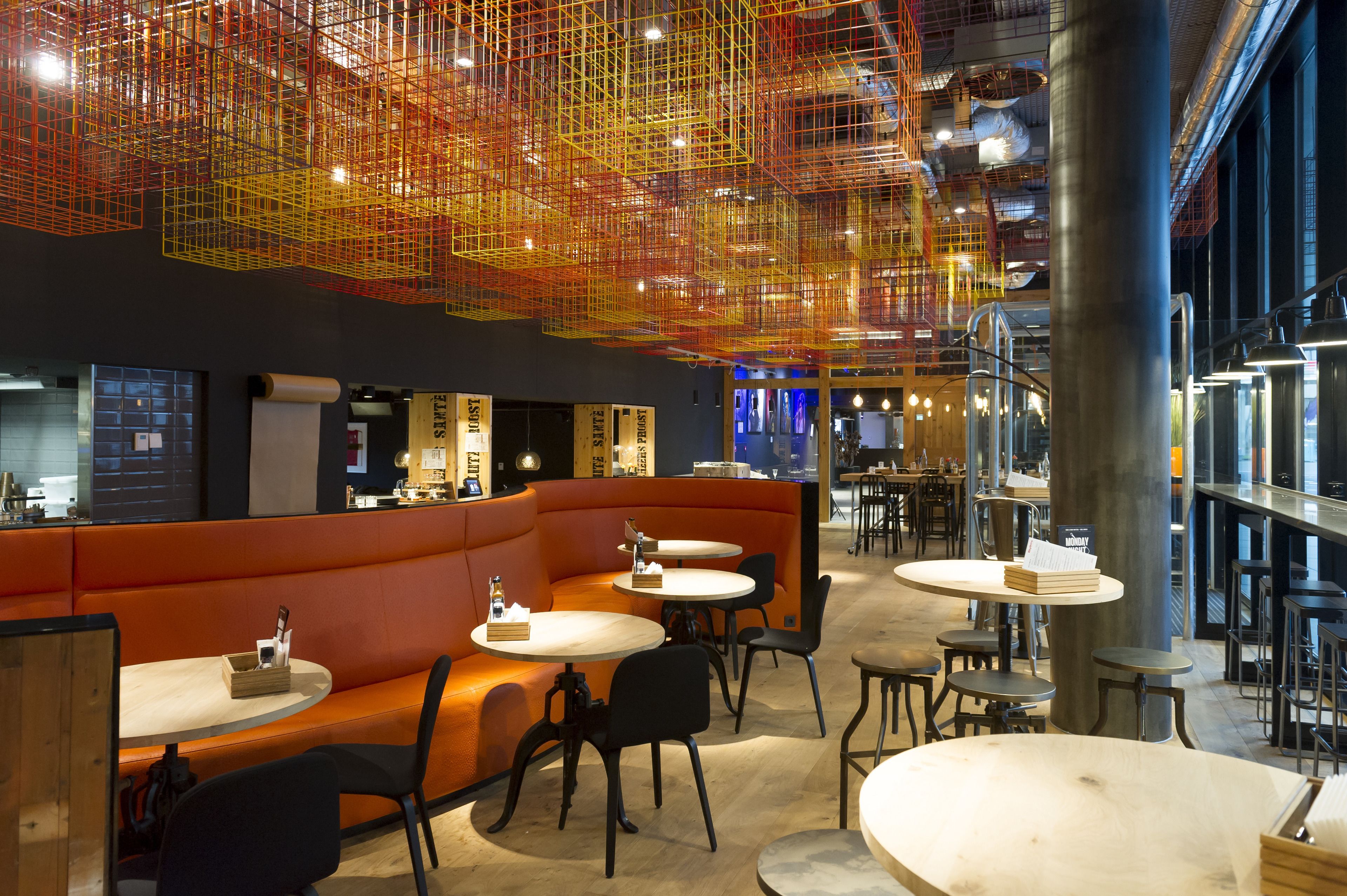A modern restaurant with orange seating, round tables, and a unique ceiling design.