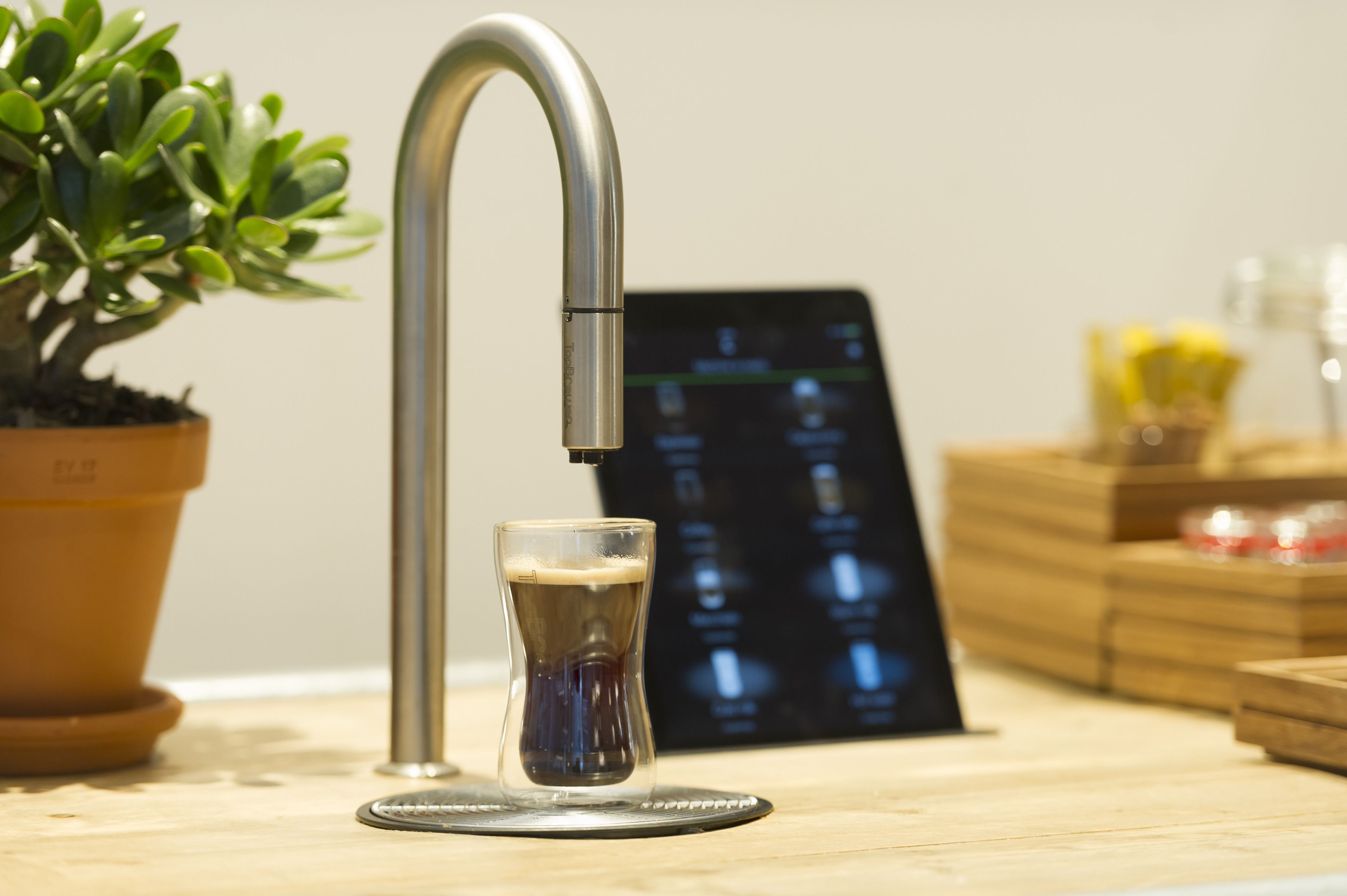 Una cocina moderna con un grifo de acero inoxidable, una cerveza en un vaso, una planta en maceta y una pantalla digital.