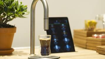 Una cocina moderna con un grifo de acero inoxidable, una cerveza en un vaso, una planta en maceta y una pantalla digital.