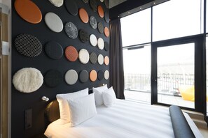 A modern hotel room with a large bed, a wall decorated with circular wall art, and a view of the city through large windows.
