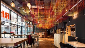 Un interior moderno con pisos de madera, sillas y mesas de metal, que destaca por un diseño de techo único con luces rojas y amarillas.