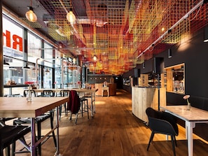 A modern interior with wooden floors, metal chairs, and tables, featuring a unique ceiling design with red and yellow lights.