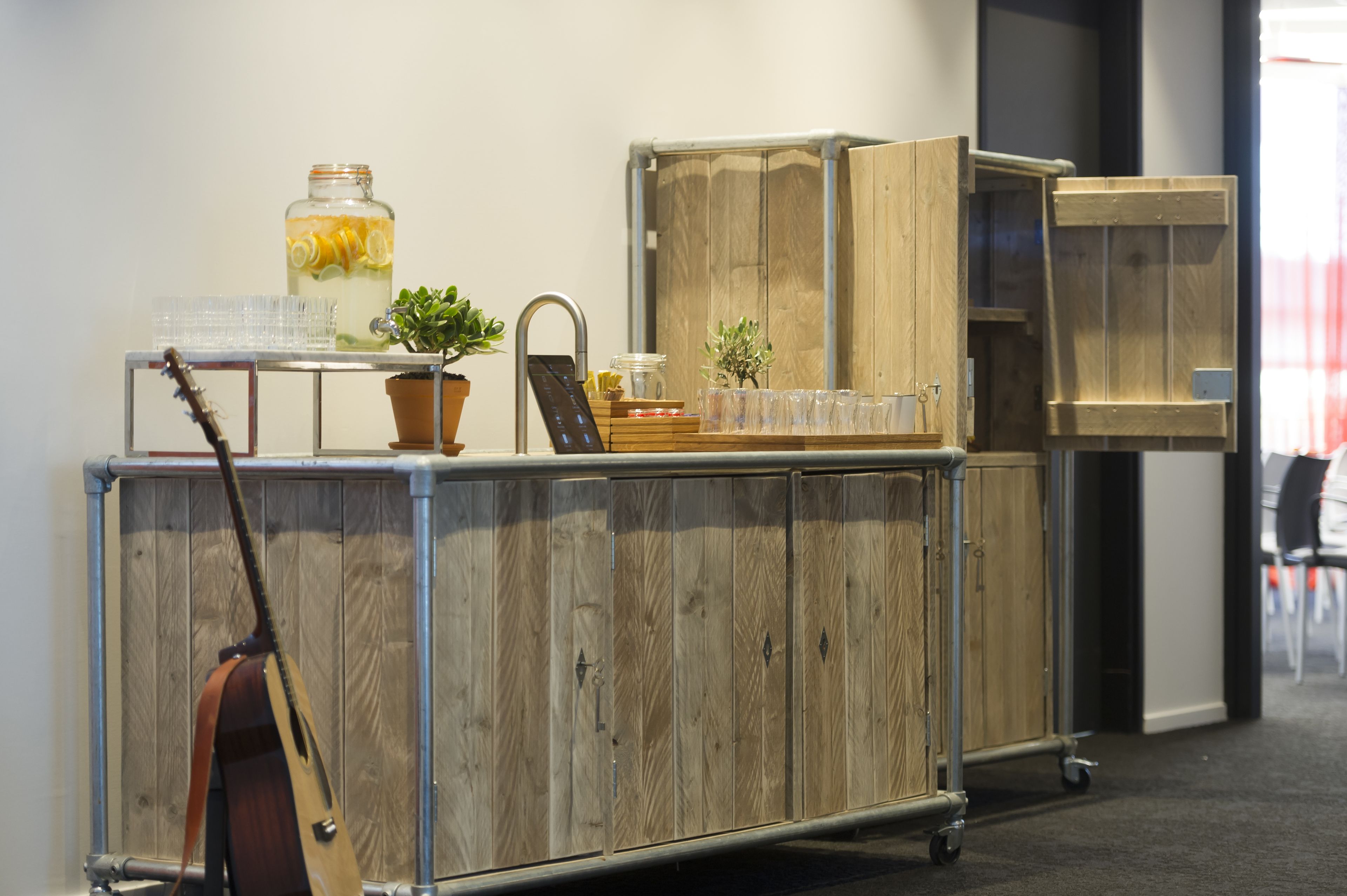 A wooden cabinet with a metal frame, a guitar leaning against it, and a small potted plant on top.