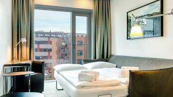 Habitación de hotel con cama, escritorio, silla y un amplio ventanal con vista a la ciudad.
